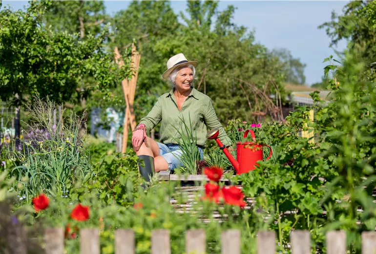 Gartenarbeit - Frau am Hochbeet mit Gießkanne